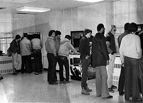 A handful of male students gather around three video game machines in Thomas Hall.